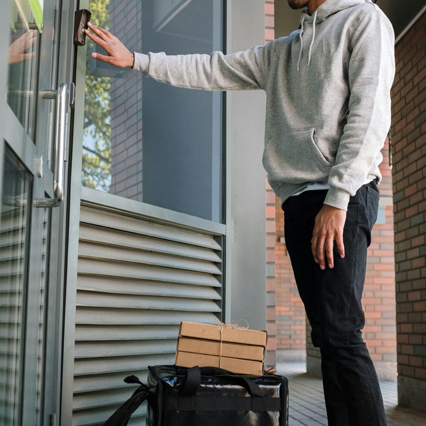 Male courier ringing doorbell for food delivery at modern building entrance.